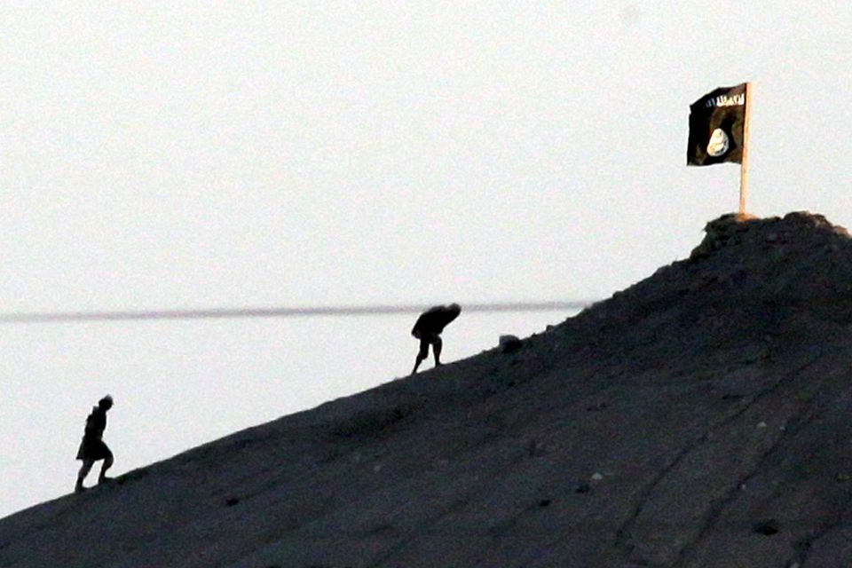 In this image shot with an extreme telephoto lens and through haze from the outskirts of Suruc at the Turkey-Syria border, militants with the Islamic State group are seen after placing their group's flag on a hilltop at the eastern side of the town of Kobani, Syria, where fighting had been intensified between Syrian Kurds and the militants of Islamic State group. AP Photo