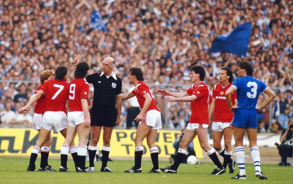 Manchester United's Kevin Moran (centre) is sent off by referee Peter Willis as United players from left to right, Gordon Strachan, Bryan Robson, Mark Hughes, Moran, Frank Stapleton and John Gidman question the decision during the 1985 FA Cup final at Wembley Stadium. Photo: David Cannon/Allpsort/Getty Images