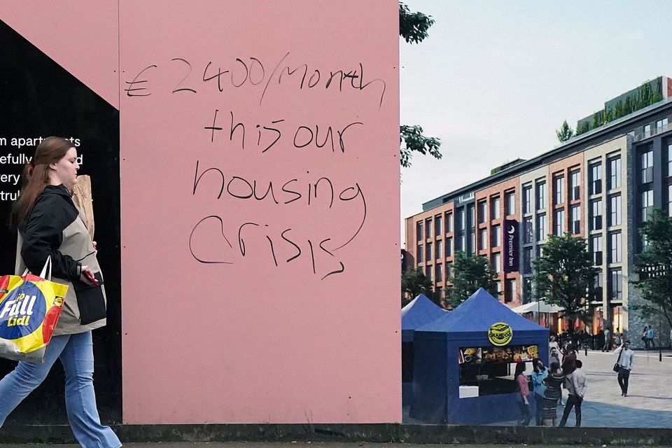 People walk past graffiti complaining about high rents on a new rental development in Dublin as property website Daft.ie reports new rents in the final three months of last year were an average of 13.7% higher than in the same period in 2021 (Niall Carson/PA)
