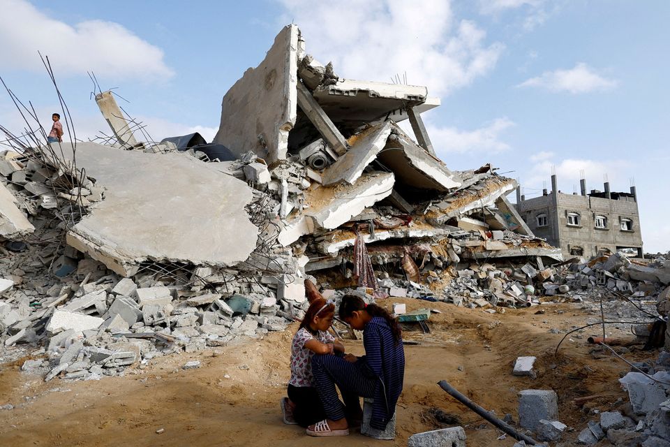 Palestinian children sit next to a building destroyed by an Israeli airstrike. Photo: Reuters