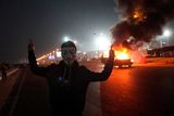 thumbnail: An Egyptian man wearing a mask of the anonymous movement gestures near a burning car outside a sports stadium in a Cairo's northeast district, on February 8, 2015 during clashes between supporters of Zamalek football club and security forces