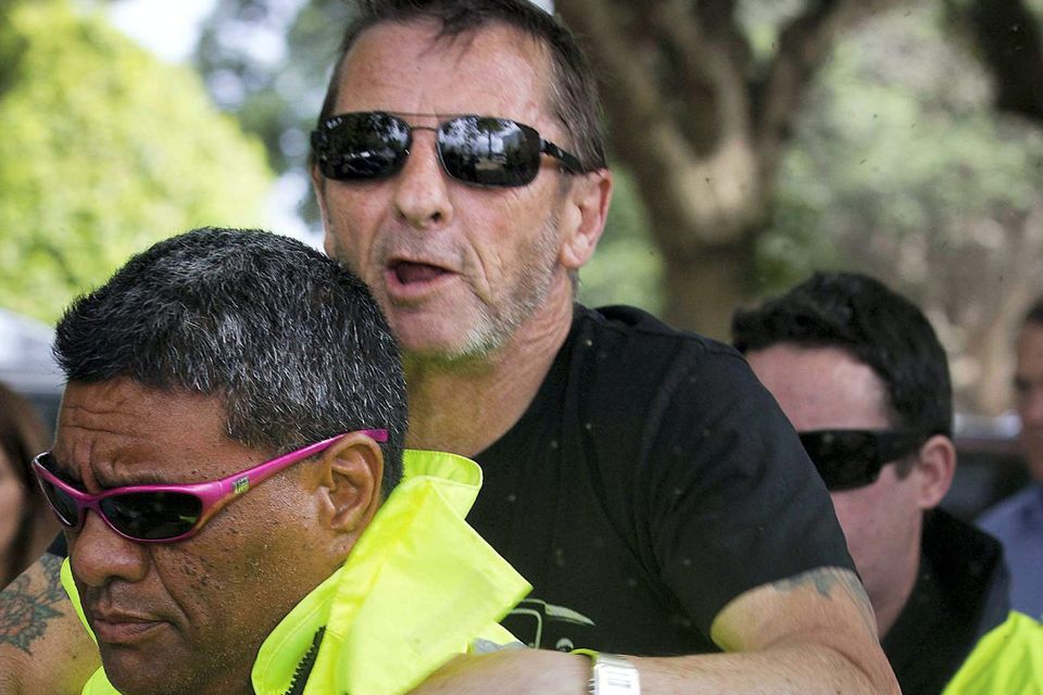 Phil Rudd drummer for the rock band AC/DC, jumps onto the back of his security guard after his short court hearing in the High Court at Tauranga, New Zealand. The 60-year-old is charged with threatening to kill, which comes with a maximum prison sentence of seven years, as well as possessing methamphetamine and marijuana. AP Photo/New Zealand Herald