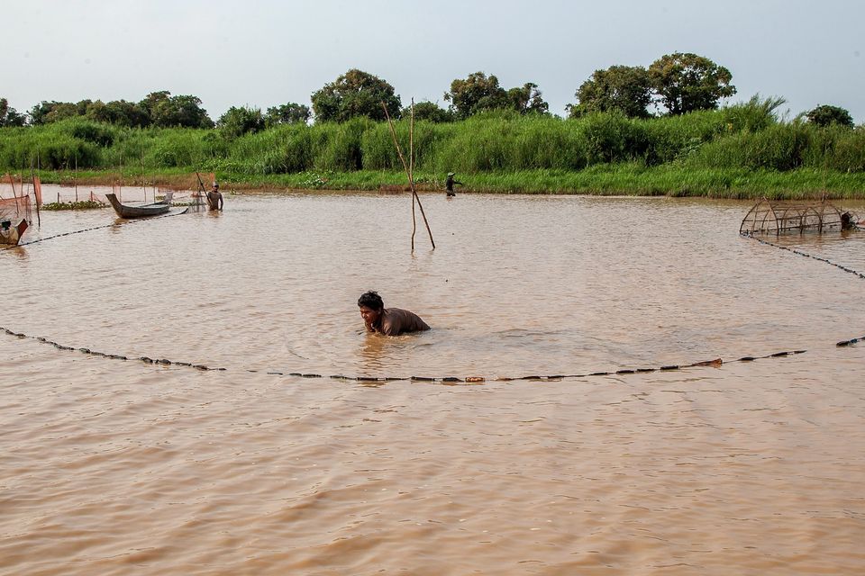 A man uses a fishing net to catch fish in the floating village