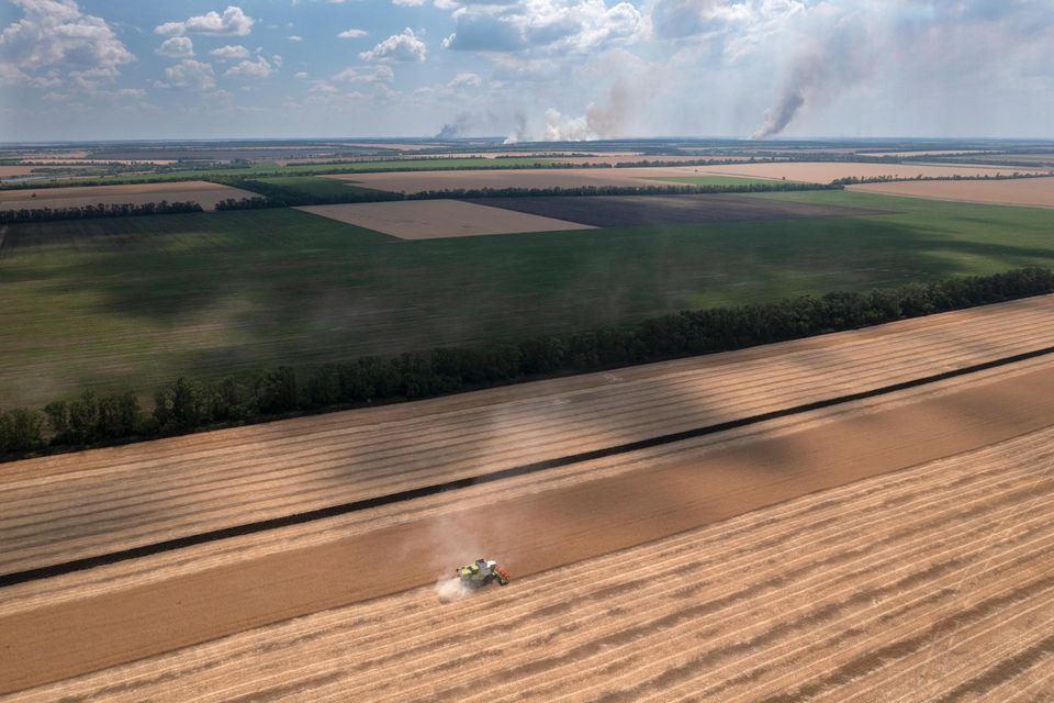 Smoke rises in the background during a fierce battle on the frontline, as a farmer collects harvest in a field in the Dnipropetrovsk region, Ukraine, Monday, July 4, 2022. . (AP Photo/Efrem Lukatsky)