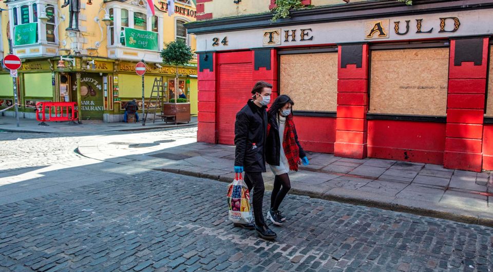 People wearing face mask as a precautionary measure against Covid-19, carry a shopping bag as the pass a boarded-up and temporarily closed pub in Dublin