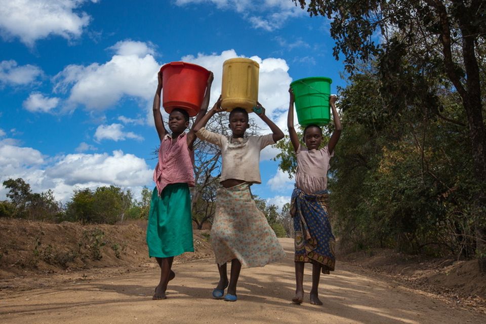 Three teenage girls carry buckets of water on a dirt road in Balaka, Malawi, where drought is a problem. Photo: Getty