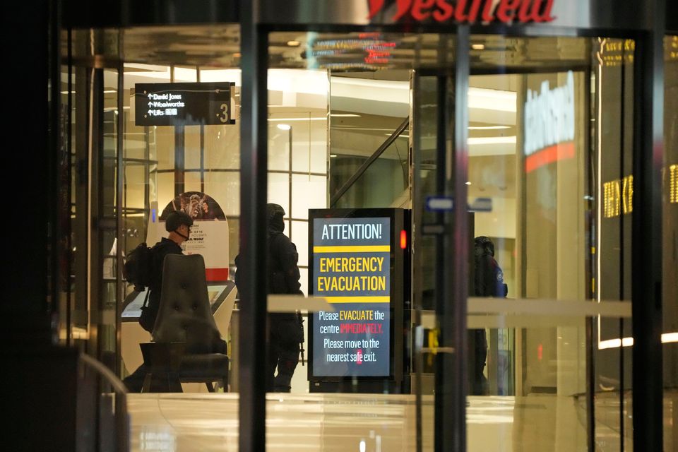 Police officers walk past a sign to evacuate at Westfield Shopping Centre, where multiple people were stabbed in Sydney (AP Photo/Rick Rycroft)