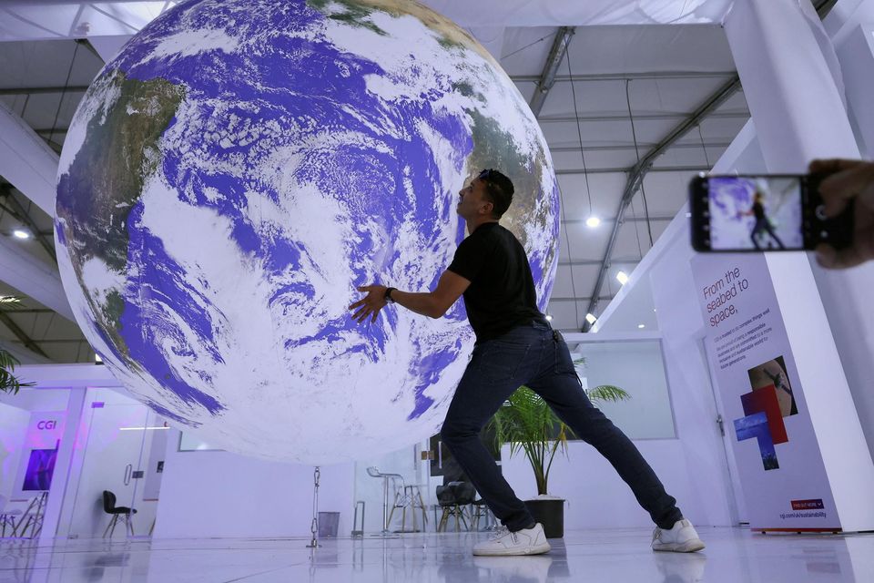 An attendee poses with a model of planet Earth at the summit in Sharm El Sheikh, Egypt. . Photo: Mohamed Abd El Ghany/Reuters