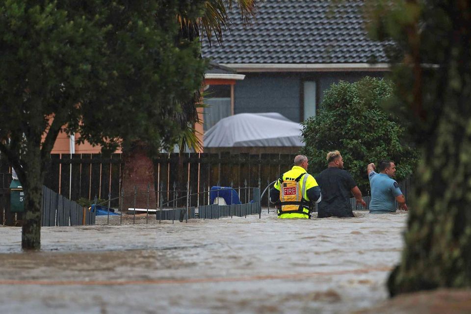 Emergency workers and a man wade through flood waters in Auckland, New Zealand. Photo: Hayden Woodward/New Zealand Herald via AP