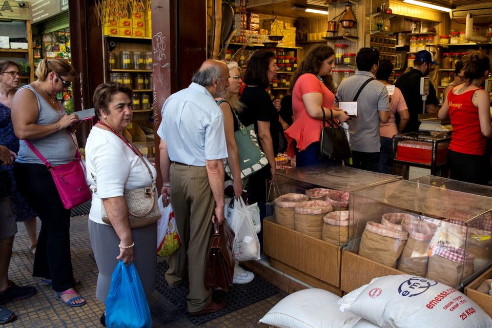People queue to buy groceries in a shop in Athens
