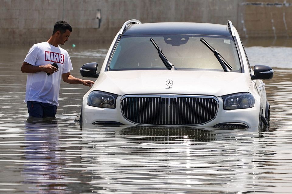 A man stands next to a car partially submerged by flood water following heavy rainfall in Dubai. Photo: Reuters