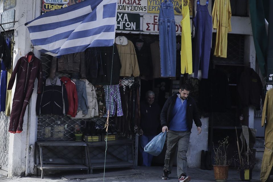 A Greek flag flies as a man leaves a clothes shop in the port city of Piraeus, near Athens (AP)