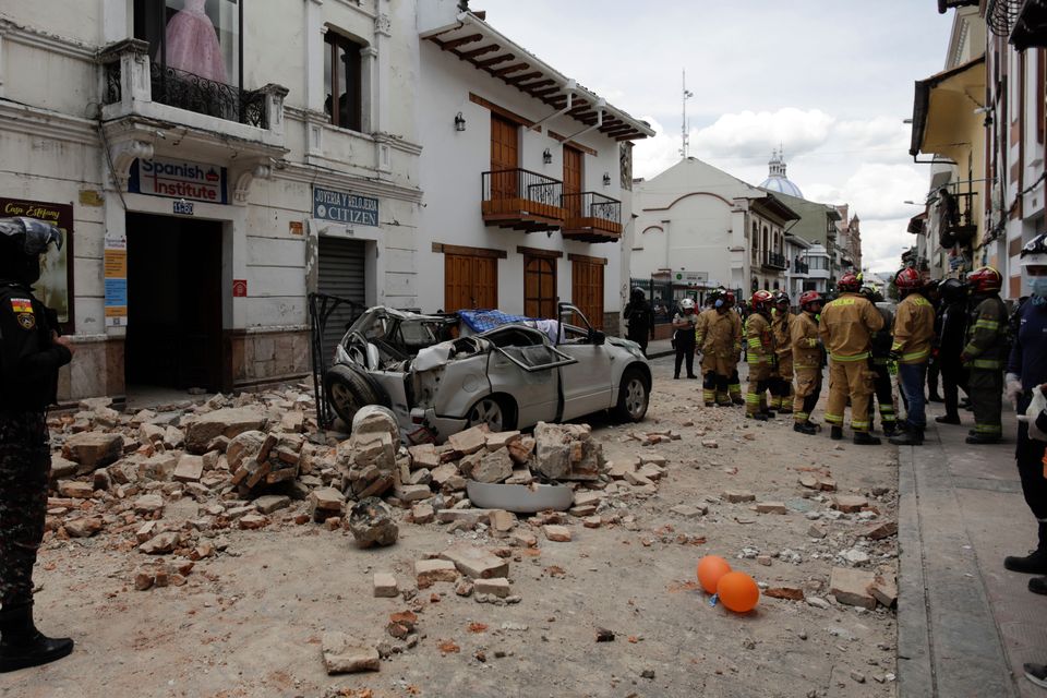 Rescue workers stand next to a car crushed by debris after an earthquake in Cuenca, Ecuador, Saturday, March 18, 2023.. The U.S. Geological Survey reported an earthquake with a magnitude of 6.7 about 50 miles south of Guayaquil (Xavier Caivinagua/AP/PA)