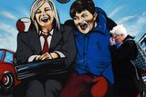 thumbnail: A woman walks past a mural depicting Sinn Fein vice president Michelle O'Neill and DUP leader Arlene Foster as the unlikely bedfellow characters from the movie Planes, Trains and Automobiles