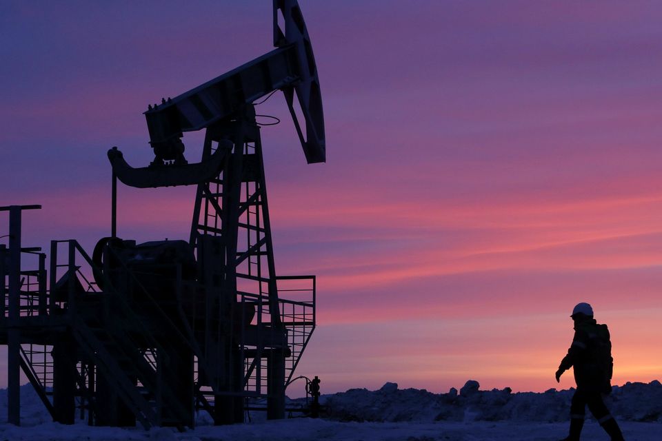 A worker walks past a pump jack on an oil field