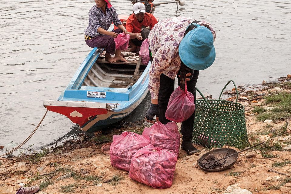 A woman buys fish from a boat near the floating village of Chong Kneas