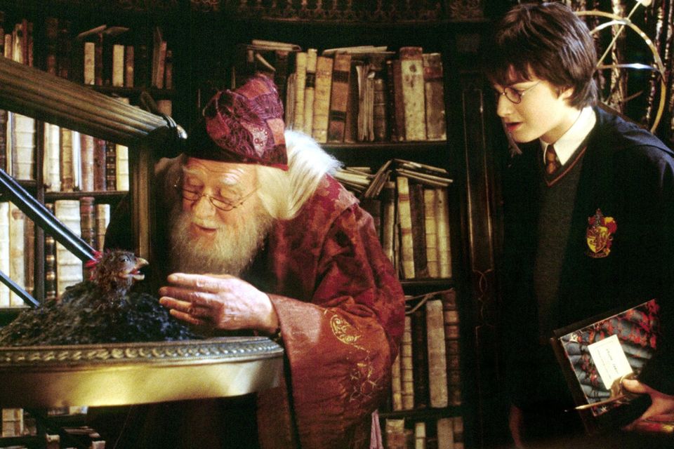 Daniel Radcliffe (R) stars as Harry Potter as he watches as Professor Dumbledore, portrayed by the late Richard Harris, feed Fawkes the Phoenix