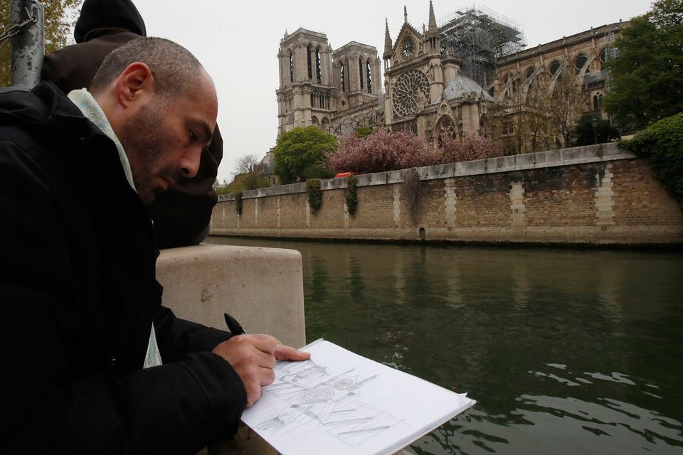 Man makes a drawing of the Notre Dame cathedral after the fire in Paris. Experts are assessing the blackened shell of Paris' iconic Notre Dame cathedral to establish next steps. Photo: AP Photo/Christophe Ena