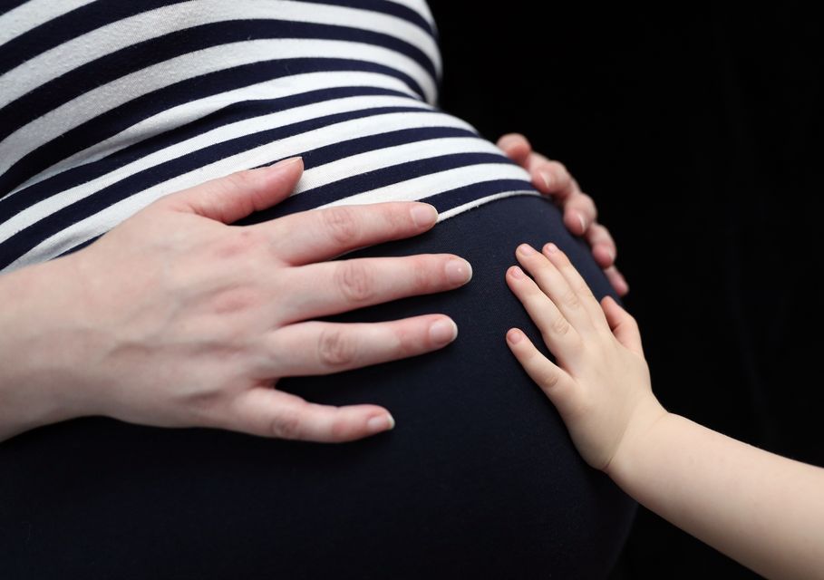 A child places a hand on the stomach of a pregnant woman.