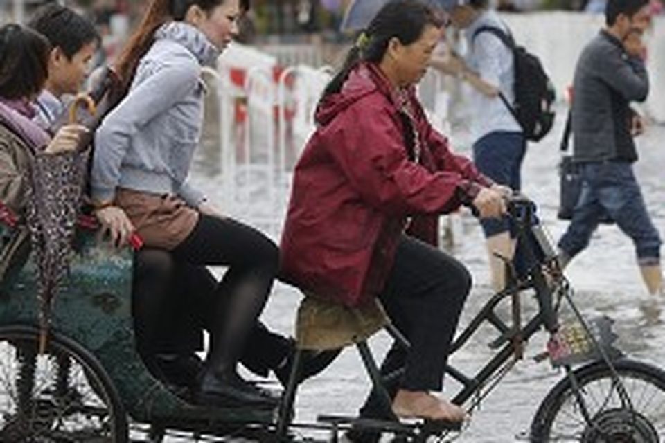 Commuters on a tricycle cross a flooded road outside a subway station in Shanghai, China (AP)