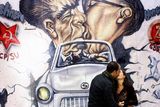 thumbnail: A couple poses to have a photo taken by a passer-by as they visit a reproduction of the Berlin Wall outside the German Embassy in Madrid
