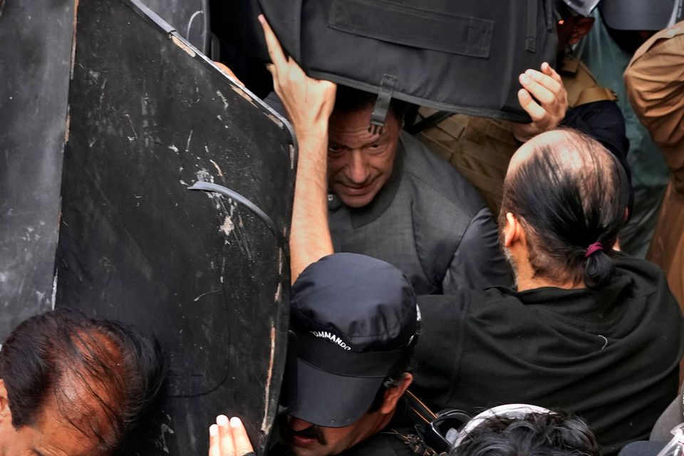 Security personnel hold bulletproof shields to secure former Prime Minister Imran Khan, center, after appearing in a court, in Lahore, Pakistan, Tuesday, March 21, 2023. A Pakistani court on Tuesday granted Khan a weeklong bail in two cases in which he faces terrorism charges, officials said. The ruling gave the embattled ousted premier and now popular opposition leader another brief reprieve from arrest. (AP Photo/K.M. Chaudary)