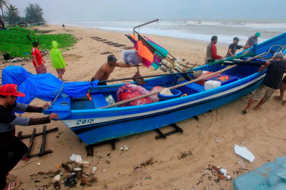 Thai men push a fishing boat off the ocean to a safer location in Songkhla, Thailand in preparation for storm weather conditions on Thursday, Jan. 3, 2019. (AP Photo/Sumeth Panpetch)