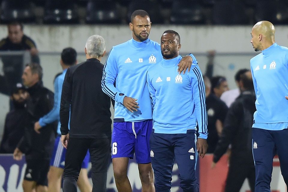 Marseille’s Patrice Evra, center right, is led away by his teammate after an incident with Marseille supporters that saw him sacked