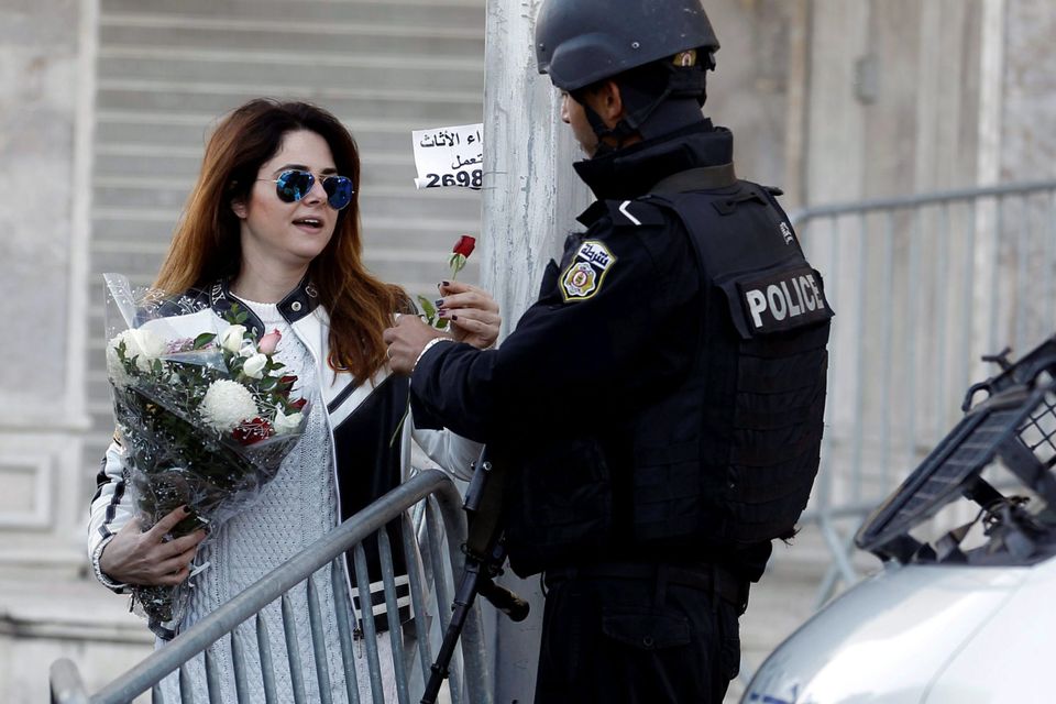 Tunisian woman gives flowers to a policeman in Tunis, Tunisia after 13 people were killed in a suicide bombing.