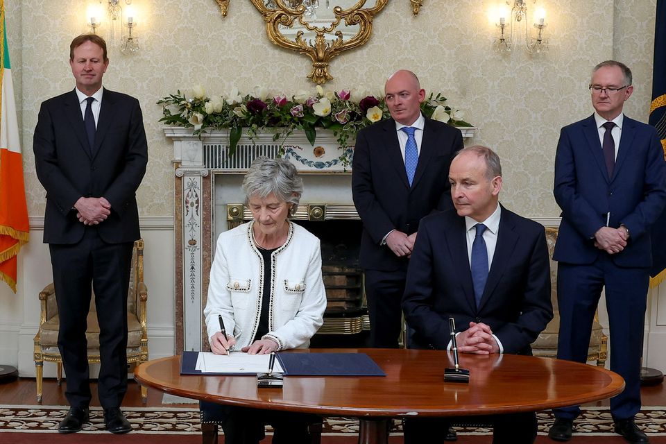 President Catherine Connolly is watched by (from left) Justice Minister Jim O’Callaghan, Attorney General Rossa Fanning, Taoiseach Micheál Martin and secretary general to the Government John Callinan as she signs the papers appointing Ms Justice Niamh Hyland and Mr Justice Brian O’Moore to the Supreme Court. Photo: Maxwells