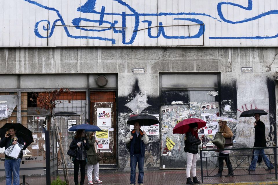 People wait for a bus in Athens under a huge slogan reading "wrong".