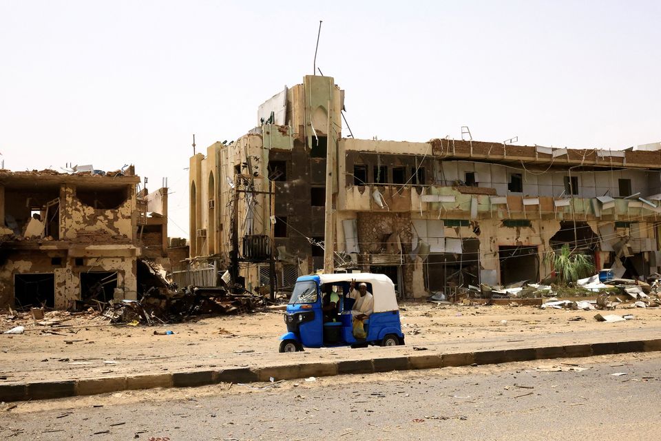 People pass by damaged cars and buildings at the central market during clashes between the paramilitary Rapid Support Forces and the army in Khartoum North. Photo: Reuters/ Mohamed Nureldin Abdallah