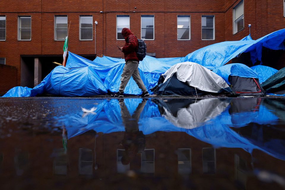 An asylum seeker walks past tents beside the IPO, where hundreds of migrants in search of accommodation have been sleeping on the streets for several months (REUTERS/Clodagh Kilcoyne)