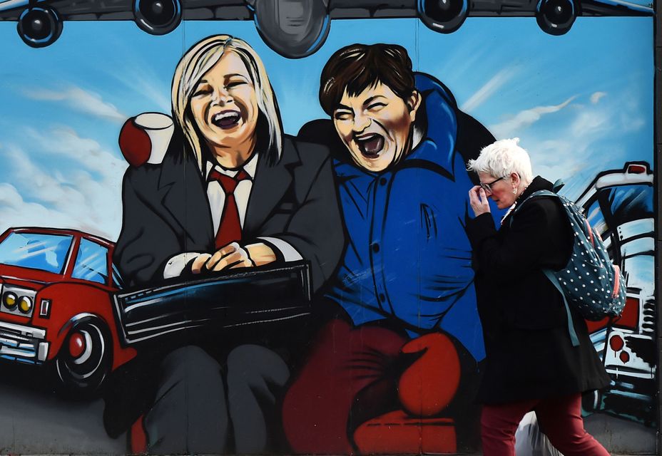 A woman walks past a mural depicting Sinn Fein vice president Michelle O'Neill and DUP leader Arlene Foster as the unlikely bedfellow characters from the movie Planes, Trains and Automobiles