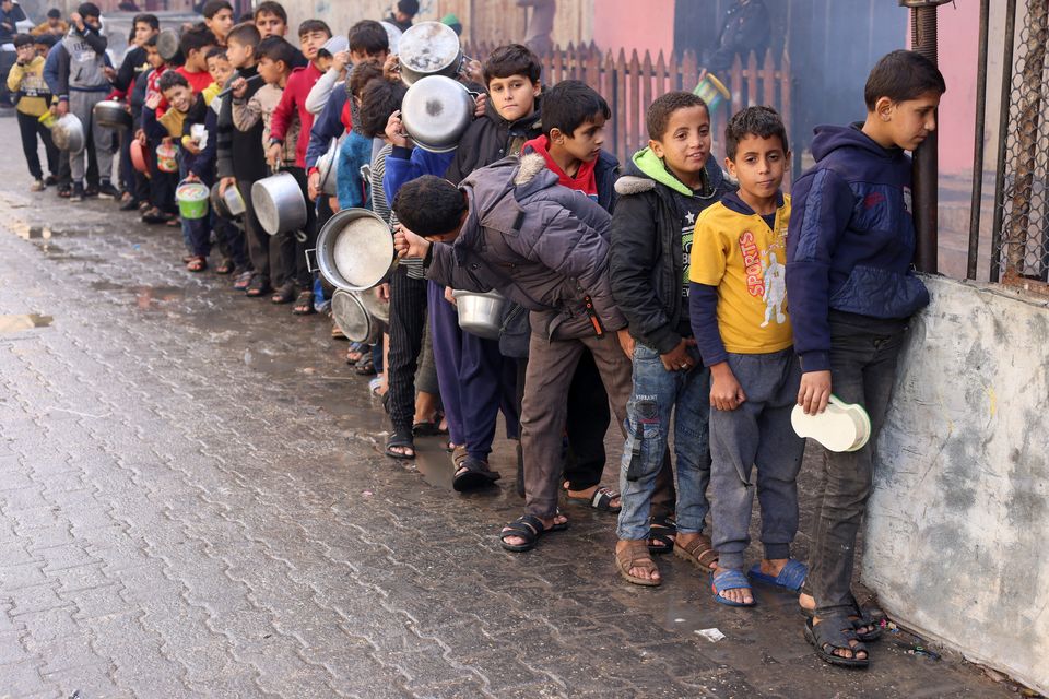 Palestinian children carry pots as they queue to receive food cooked by a charity kitchen, amid shortages in food supplies, as the conflict between Israel and Hamas continues, in Rafah in the southern Gaza Strip December 14, 2023. REUTERS/Saleh Salem