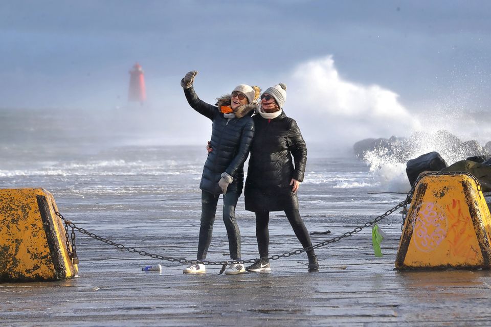 Walkers at the South Bull Wall as high winds churn up the sea during high tide