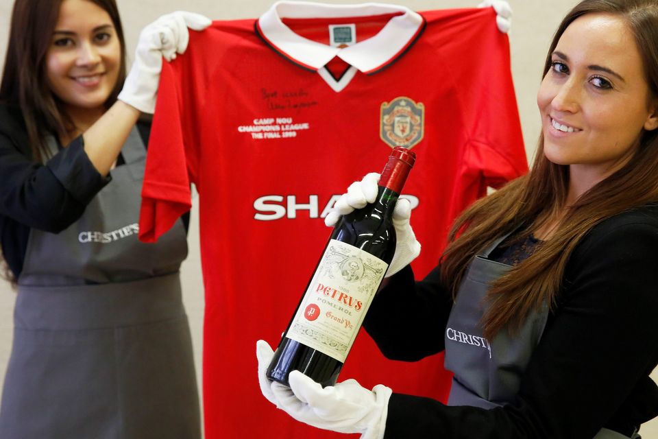 Christie’s staff with a bottle of Petrus 1988 and a Manchester United retro Champions League shirt from 1999. Reuters