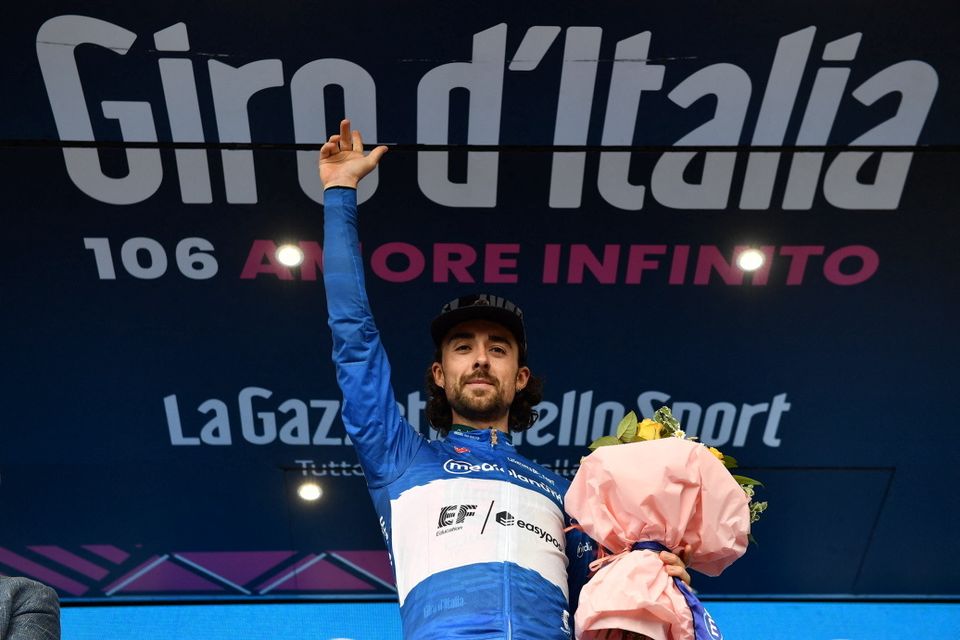 Ben Healy celebrates on the podium wearing the maglia azzurra jersey after stage 16