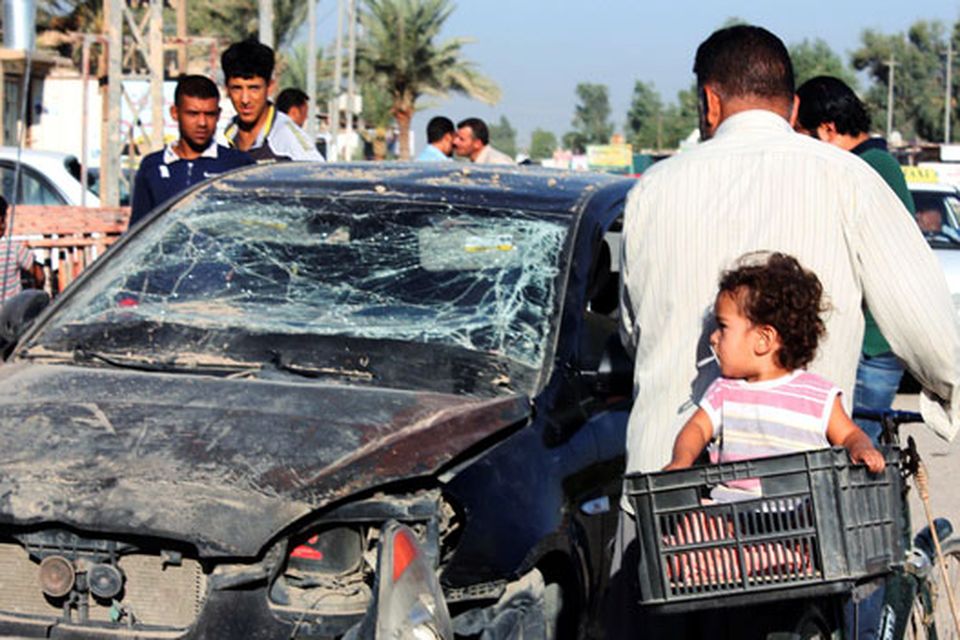 Residents pass by a damaged vehicle a day after a bomb attack in central Baquba, 65 km (40 miles) northeast of Baghdad