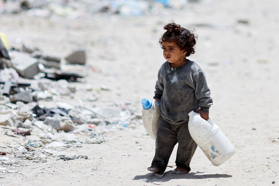 A little Palestinian girl carries containers to collect water as she walks by houses that were destroyed in an Israeli strike in the southern Gaza Strip. Photo: Reuters