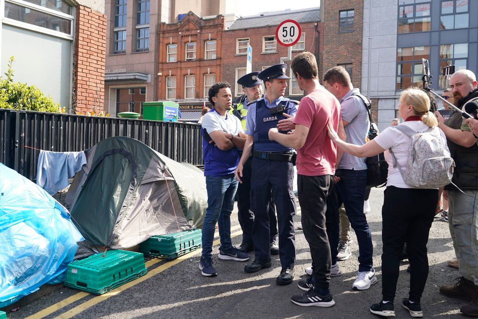 A homeless man by his tent as gardaí engage with marchers outside the  International Protection Office in Dublin on Saturday. Photo: Niall Carson/PA