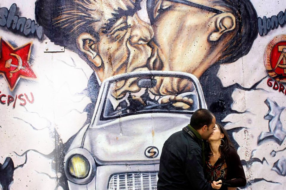 A couple poses to have a photo taken by a passer-by as they visit a reproduction of the Berlin Wall outside the German Embassy in Madrid