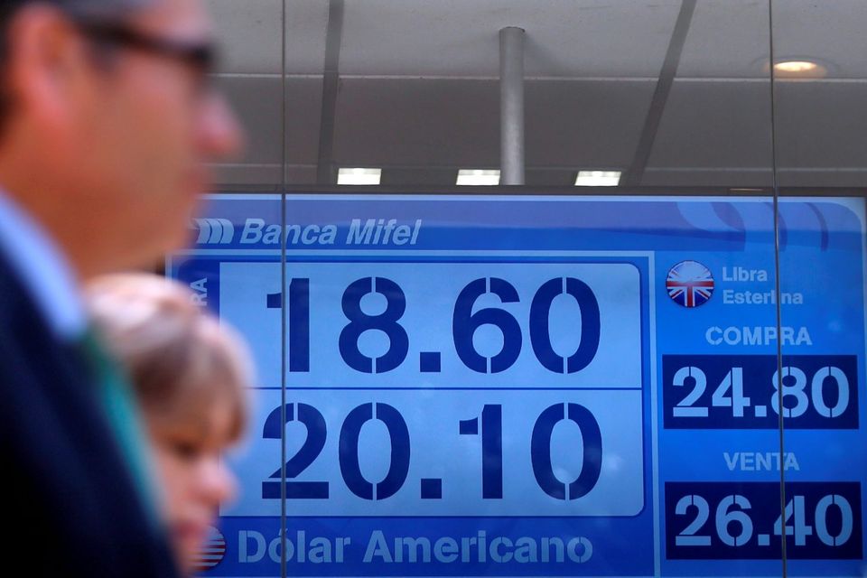 People pass in front of a board displaying the exchange rate for peso and US dollars at a foreign exchange house in Mexico City