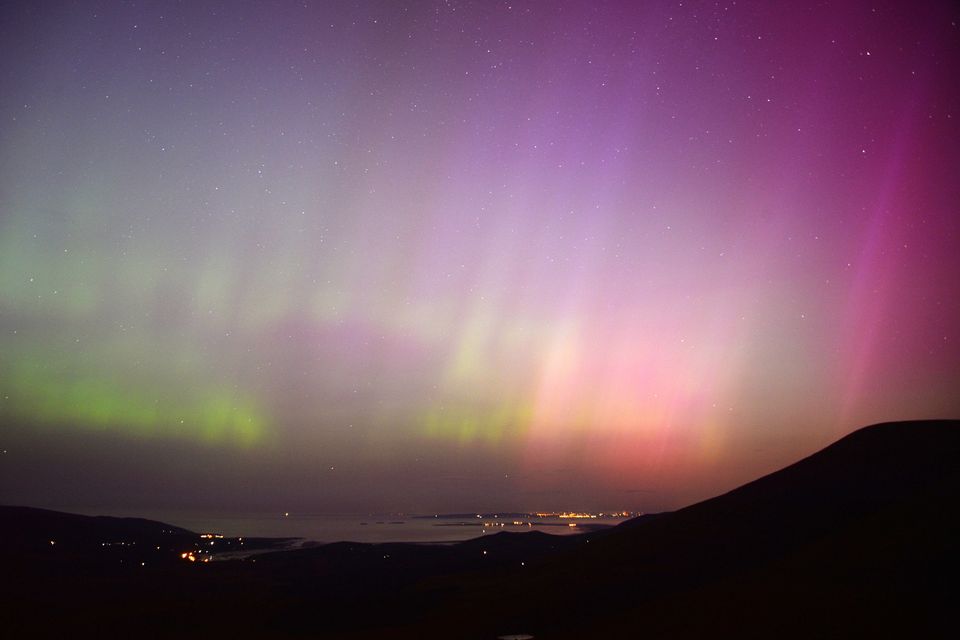 La aurora boreal sobre la bahía de Tralee vista desde la cima de Conor Pass alrededor de las 2 a.m. del sábado por la mañana.  A simple vista se ve un tenue resplandor en el cielo, pero la cámara revela todo el espectro de colores producidos por la tormenta solar.  Foto de Declan Malone.
