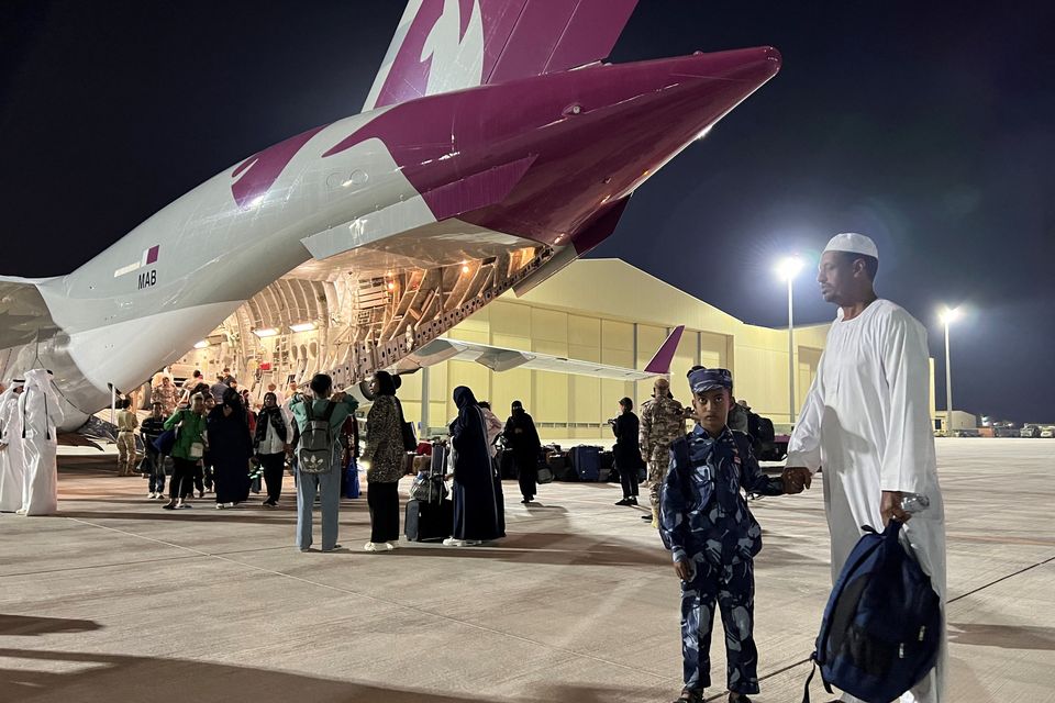 A Sudanese boy with his father next to a military aircraft in Qatar, after being flown in from Port Sudan. Photo: Reuters