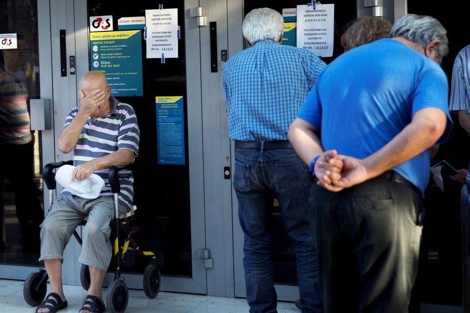 A elderly man In a wheelchair waits with other pensioners outside a national bank branch to withdraw a maximum of €120 ($134) for the week in central Athens