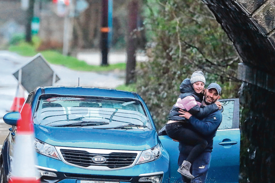 A motorist carries his child through flood water after his car got stuck on the Piltown Road in Bettystown, Co Meath
