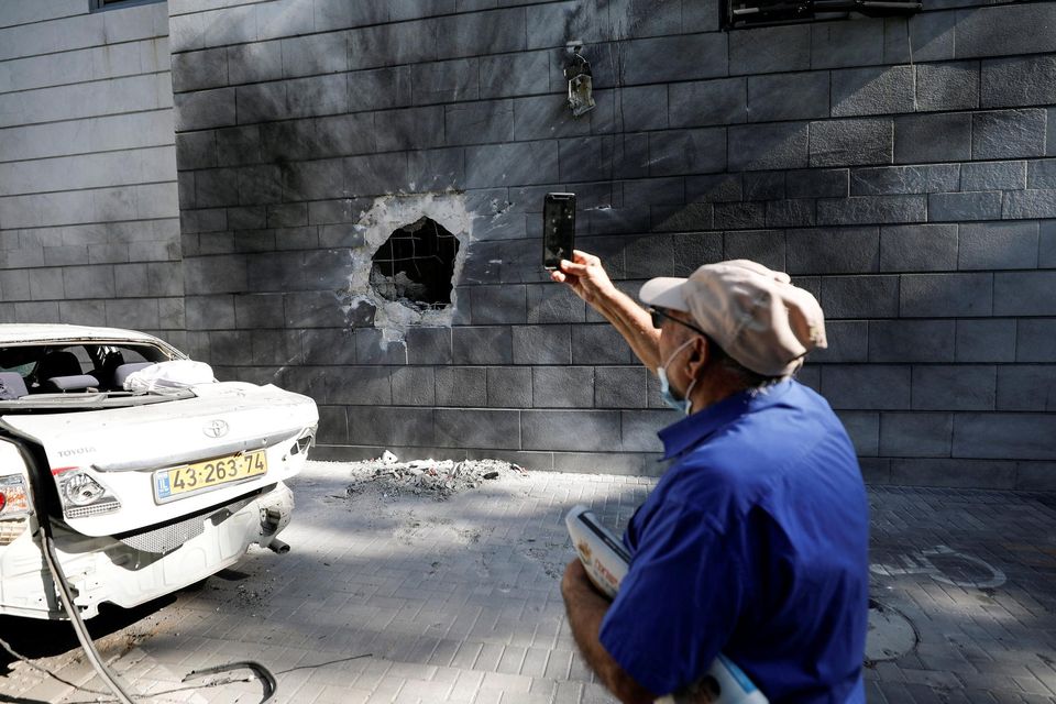 An Israeli man takes a photo with his mobile phone at a residential building after a rocket launched overnight from the Gaza Strip hit it in Ashkelon. Picture: Reuters