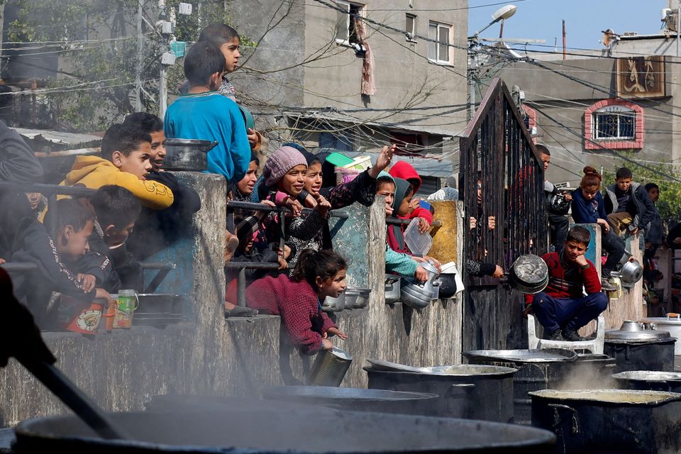 Palestinian children wait to receive food cooked by a charity kitchen in Rafah. Photo: Reuters