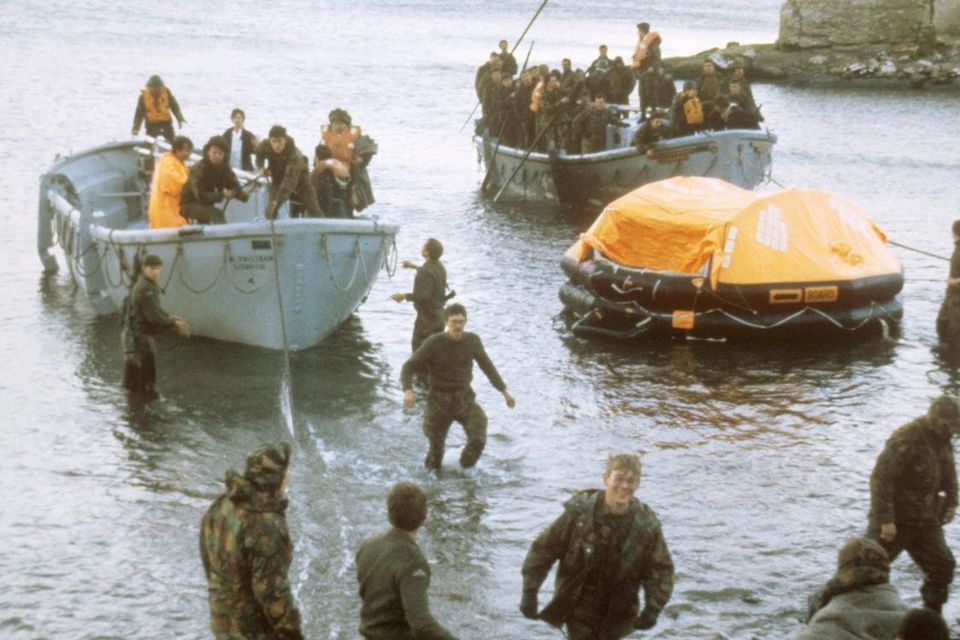 Sir Galahad survivors coming ashore in life rafts at San Carlos Bay after an air attack on the supply ship, which blazes in the background, during the Falklands war in 1982